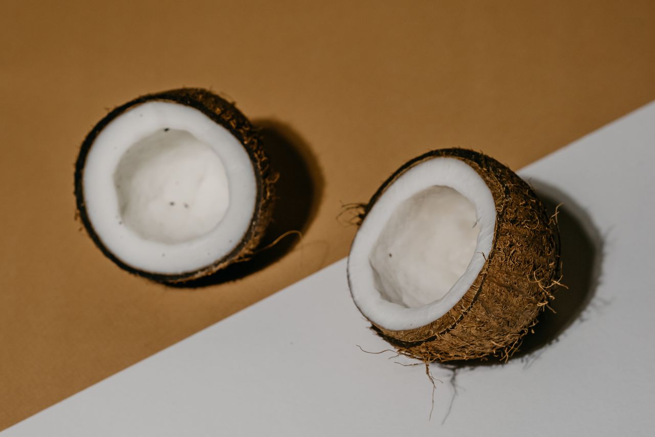 Halved coconuts on a brown and white background, showcasing the texture and freshness of the fruit.